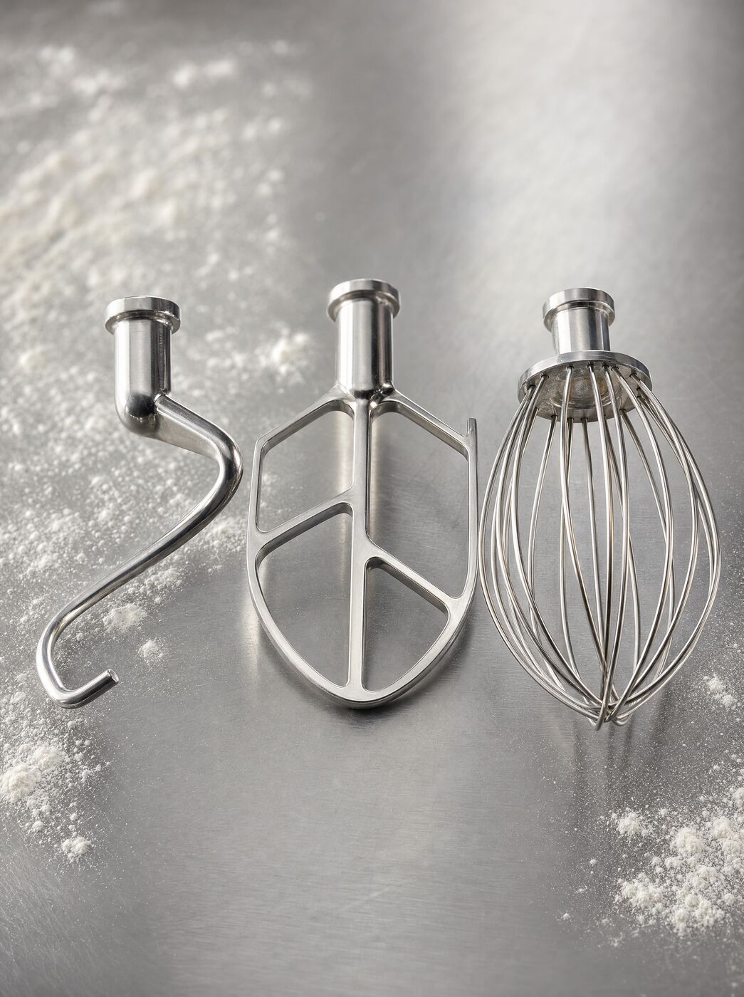 The dough hook, flat beater and wire whisk laid on a stainless bench